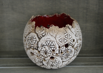 Rundes weißes Keramikgefäß mit sternförmigem Relief, mehreren Durchbrüchen und roter Innenfläche.