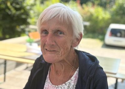 Porträt einer lächelnden Teilnehmerin des ViWo Grillfests 2025, sitzend im Freien an einem Tisch, trägt helles gemustertes Oberteil und dunkle Jacke.
