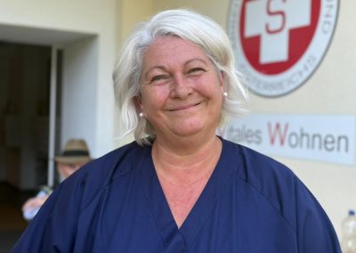 Lächelndes Porträt einer Frau in blauer Dienstkleidung mit Namensschild ‚Samariterbund ViWo‘, im Hintergrund das Logo des Samariterbundes.