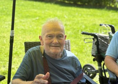Älterer Mann sitzt im Freien, hält einen Teller mit Kuchen; Rollator im Hintergrund.