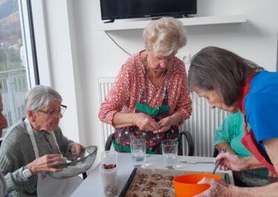 Drei ältere Frauen formen Kekse an einem Tisch mit Backblech, Ausstechformen und Schüsseln.