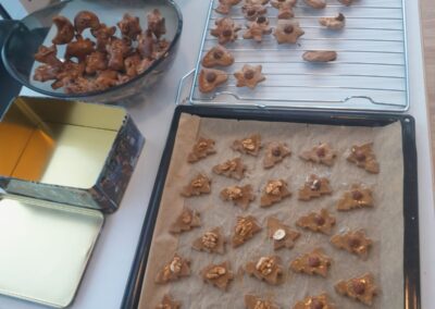 Backblech und Abkühlgitter mit vielen Plätzchen in Stern-, Herz- und anderen Formen, jeweils mit Nüssen belegt; Schalen und Keksdose daneben.