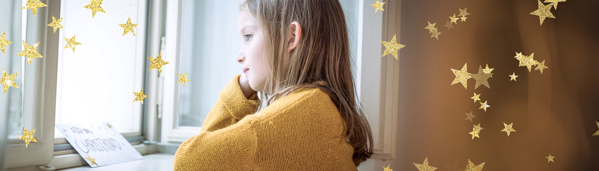 Kind in gelbem Pullover schaut aus dem Fenster; Zettel auf der Fensterbank mit der Aufschrift "Für's Christkind"; goldene Stern-Overlays