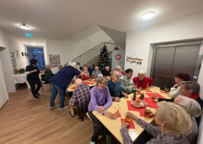 Ältere Menschen sitzen an Tischen in einem Innenraum mit Weihnachtsbaum und einem Banner mit der Aufschrift 'Samariterbund Bad Ischl'.