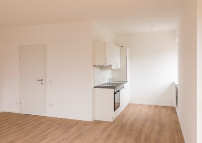 Unmöblierter Wohnraum mit kleiner weißer Küchenzeile und Holzfußboden