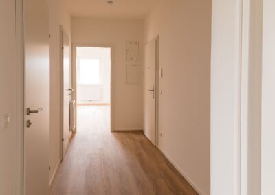 Leerer Wohnungsflur mit Holzboden, mehreren Türen und hellem Fenster am Ende.