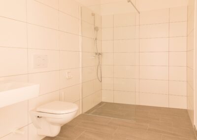 Gefliestes Badezimmer mit begehbarer Dusche, Glasabtrennung, Handbrause und Wand-WC
