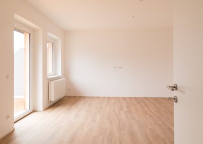 Leerer Innenraum mit weißen Wänden, Holzfußboden, Fenstern und Heizkörper.